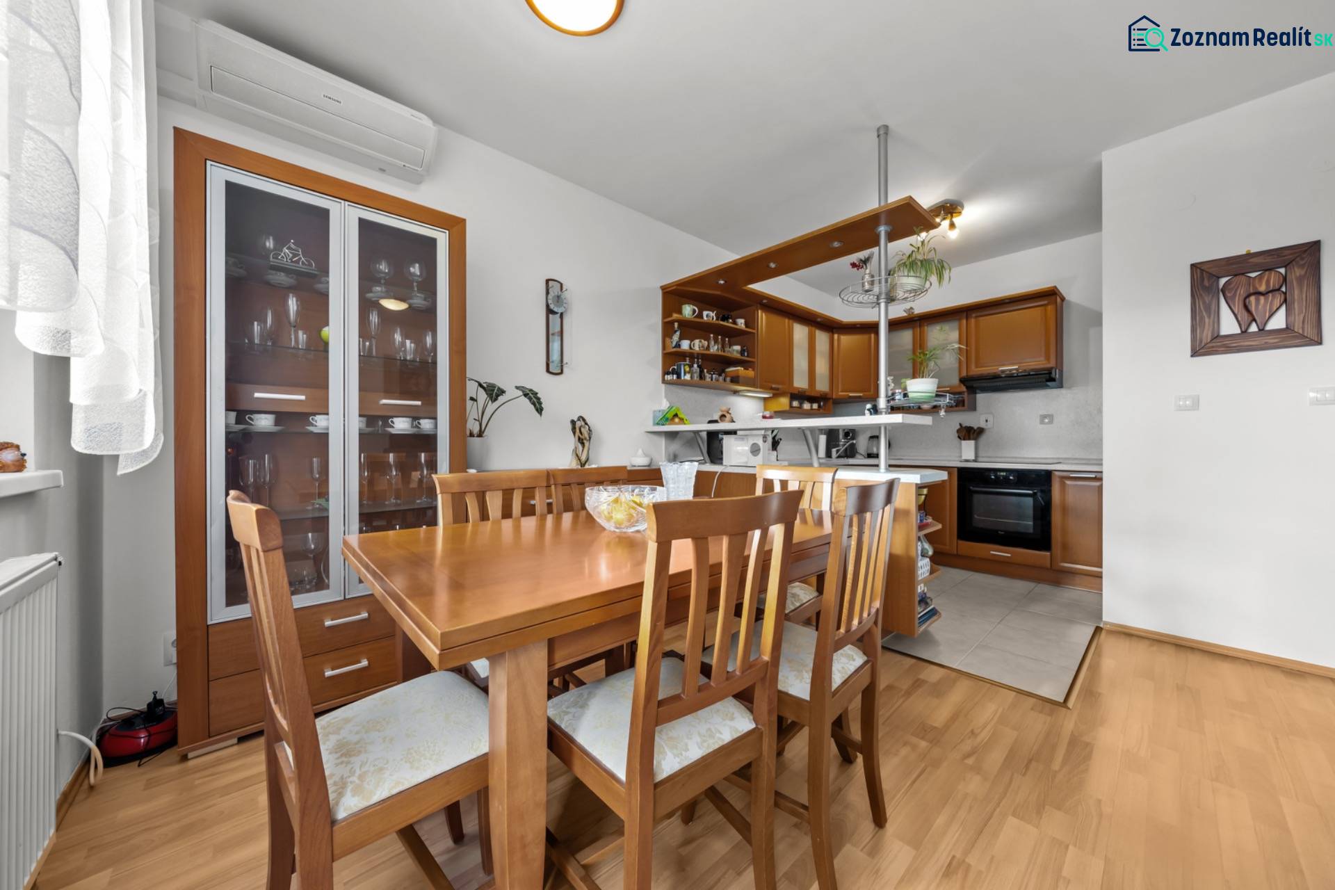 Dining area with wooden furniture and a kitchen in a 4-room apartment with a wood-patterned floor.