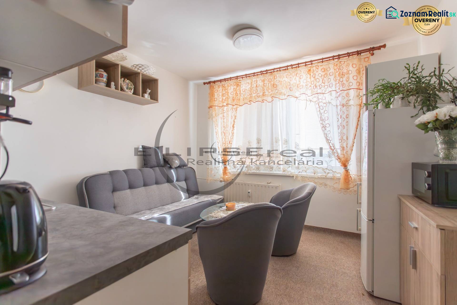 A kitchen in a studio apartment with a gray sofa and decorative curtains.