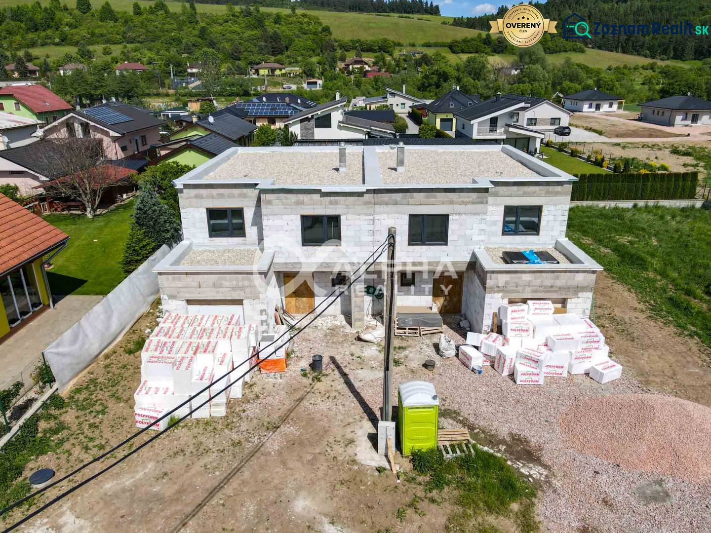 A family house under construction in Harichovce, surrounded by greenery and other houses.
