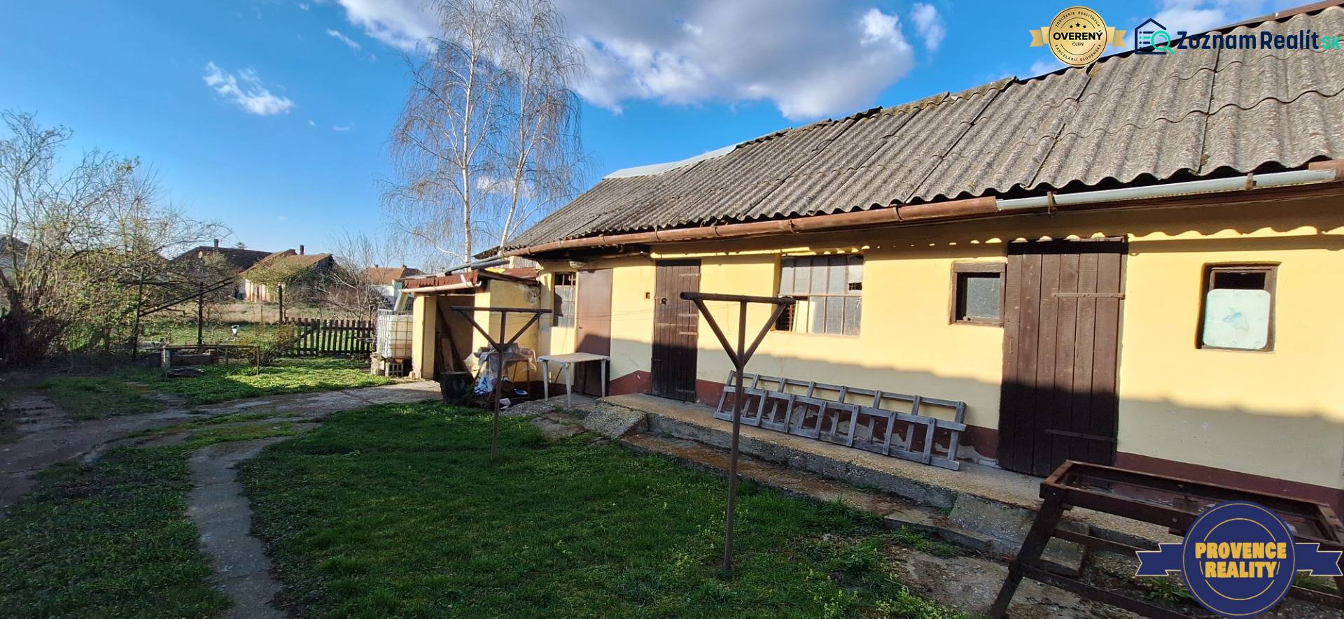 A family house in the village of Holiare with a lawn, trees, and a wooden shelter.