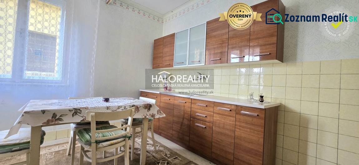 A kitchen in a family house, equipped with a dining table, chairs, and windows with white curtains.