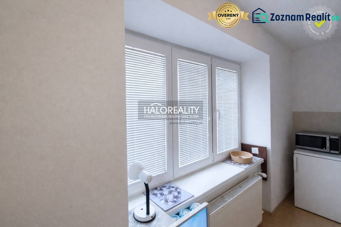 A studio apartment with white blinds and a microwave on a shelf.