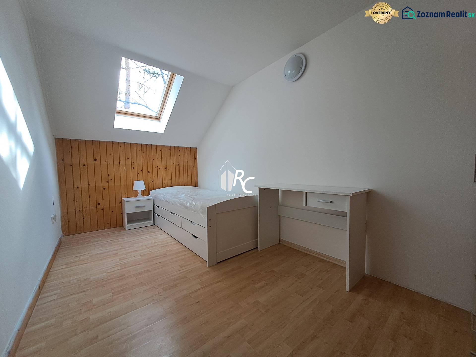 A bright room with a bed, a desk, a skylight, and a wooden floor.