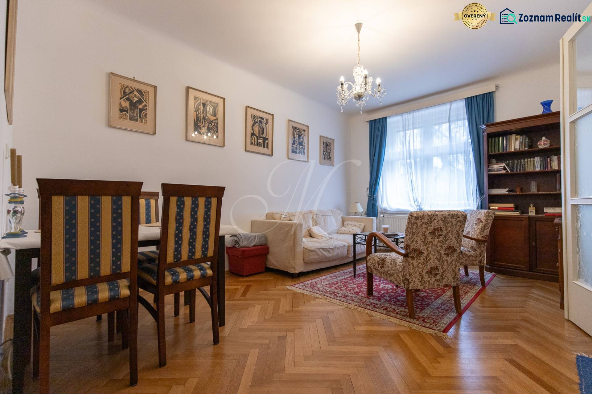 Living room with a sofa, bookshelf, chairs, wooden decor flooring, and a chandelier in a three-room apartment.
