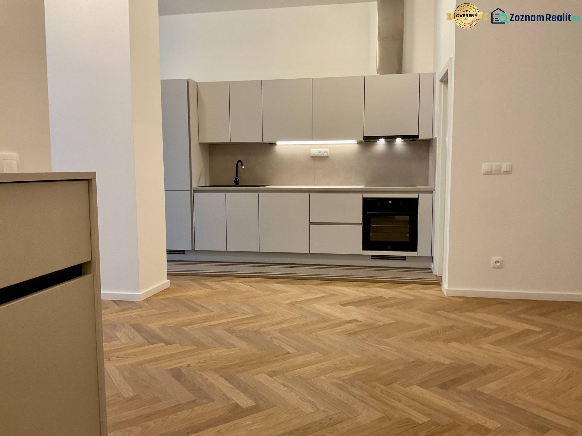 A kitchen in a 2-room apartment with a wood-patterned floor and light cabinets.