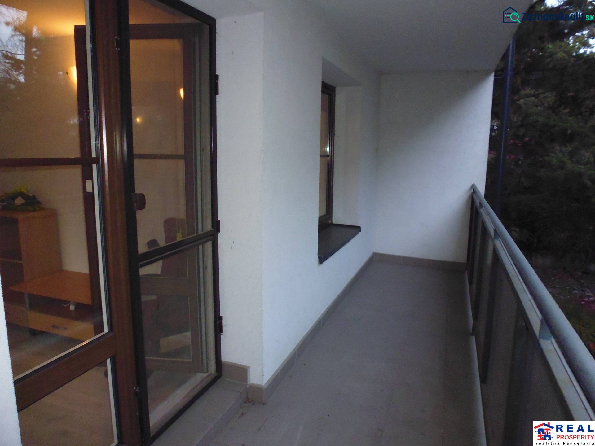A balcony of a 2-room apartment with a view of the surrounding greenery, access through glass doors.