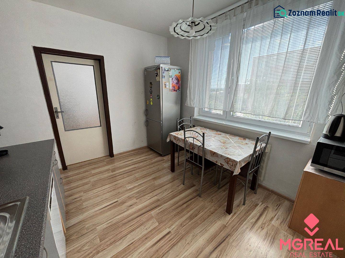 A kitchen in a 3-room apartment with a wooden decor floor, a dining table, and appliances.