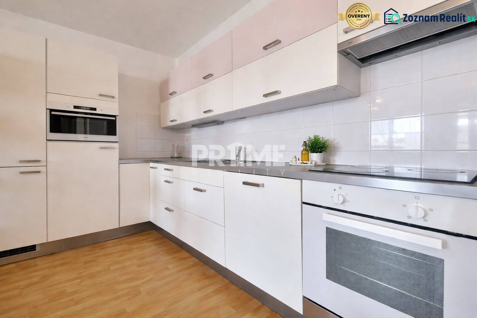 A kitchen unit in a 2-room apartment with a wooden decor floor and white cabinets.