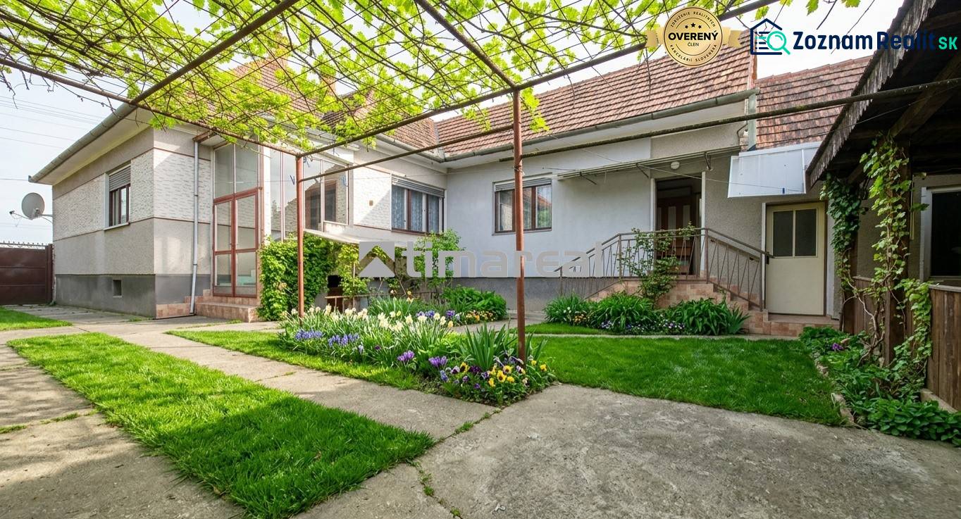 A family house in Trstín with a front garden, vine, and flower planting.