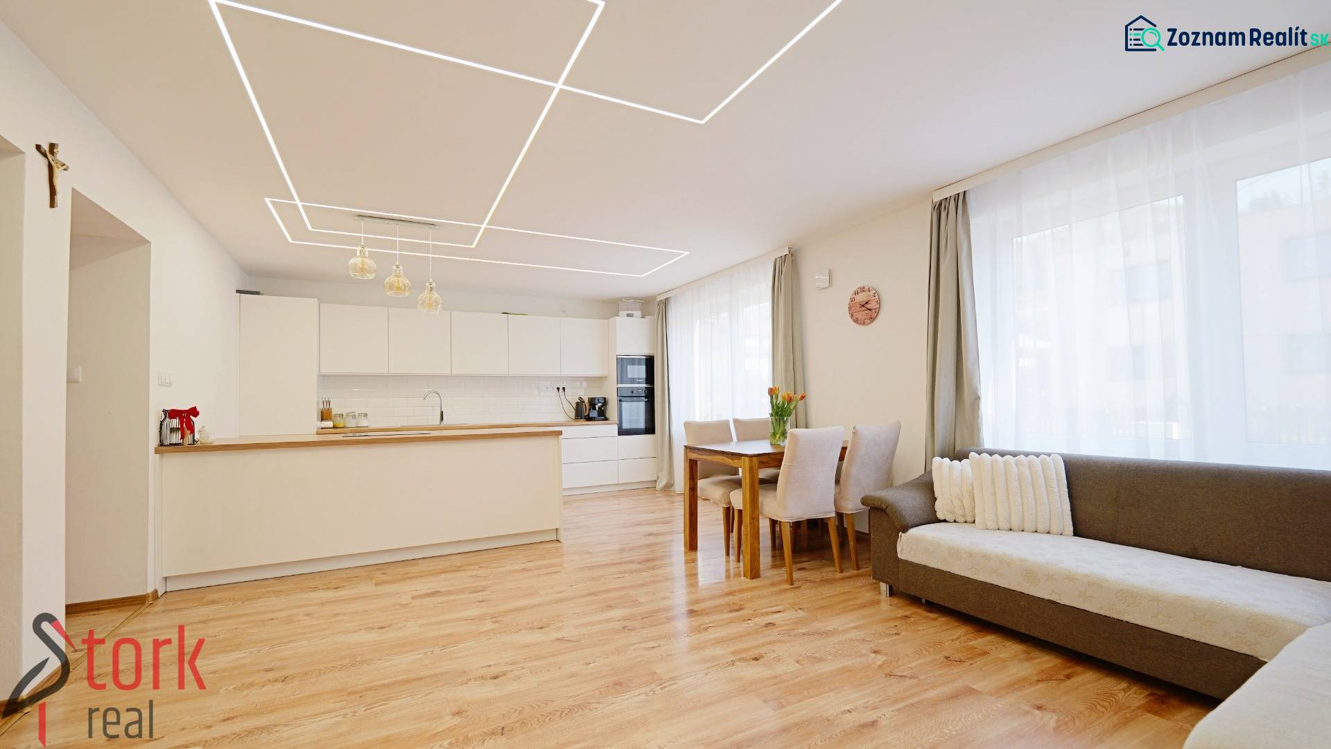 Interior of a family house with a kitchen and living room, wooden decor flooring, and light-colored furniture.