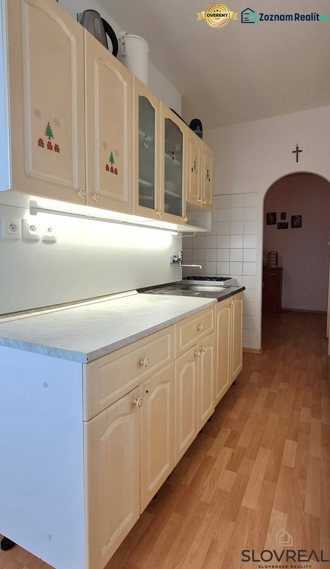 A kitchen in a 2-room apartment with a wooden decor floor and an arched transition.