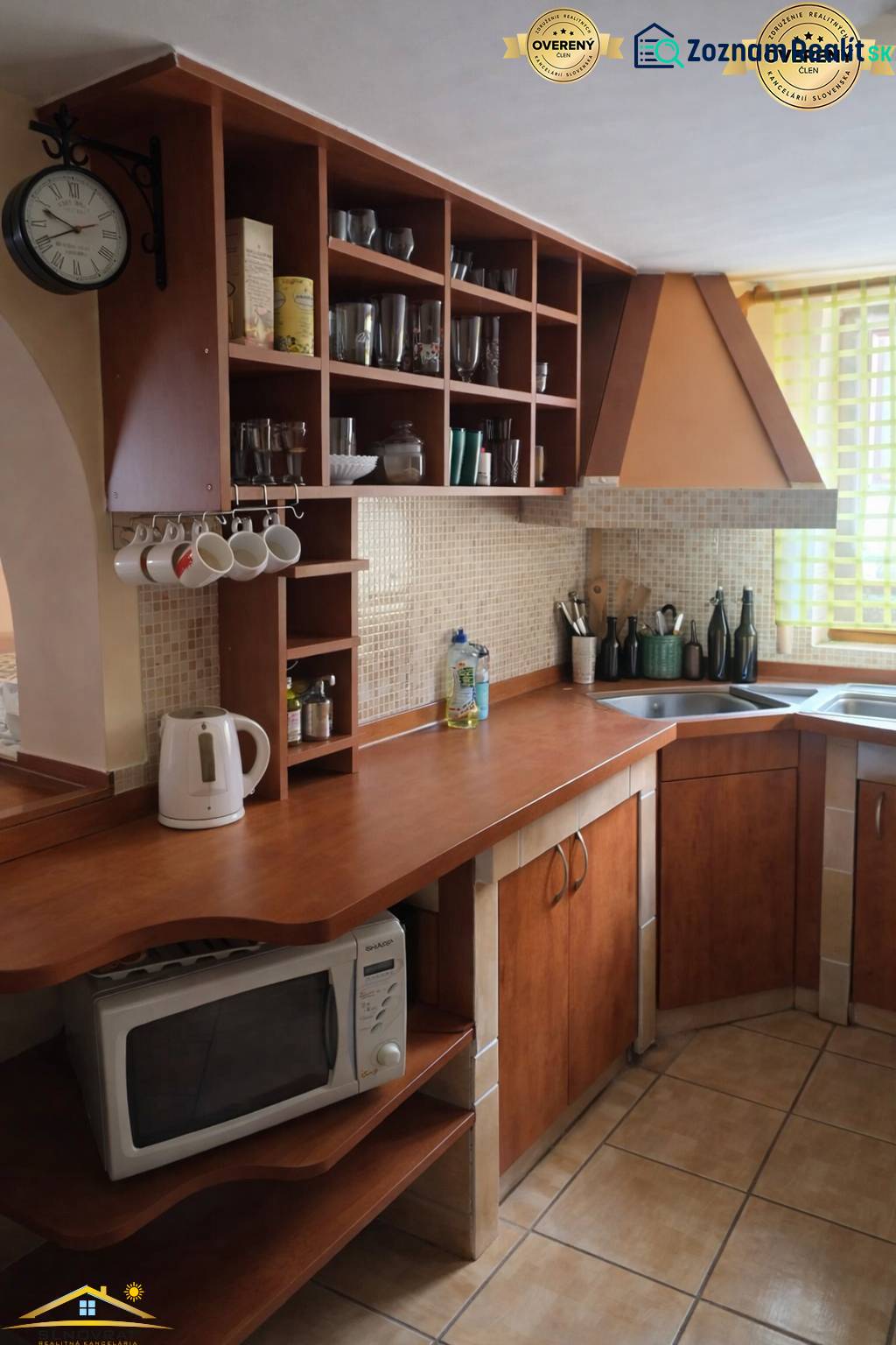 A kitchen in a family house with wooden cabinets and shelves, complemented by a wall clock.