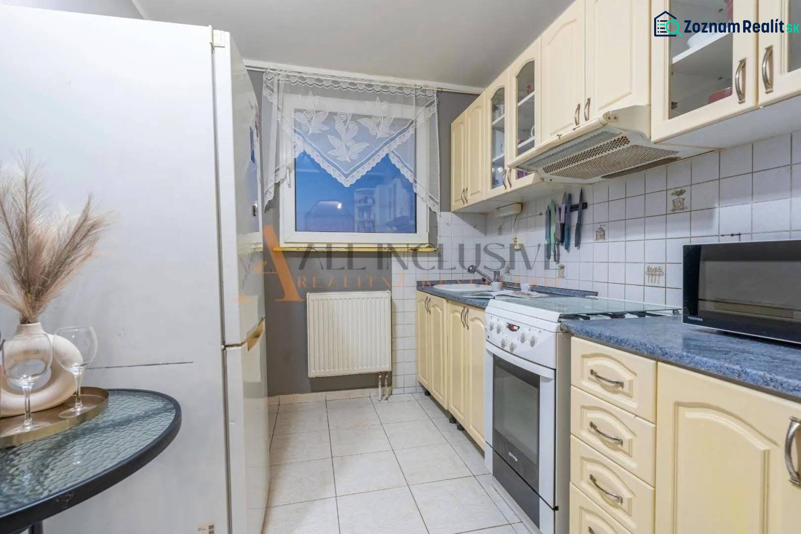 A kitchen in a 3-room apartment with white tiles, appliances, and a table.