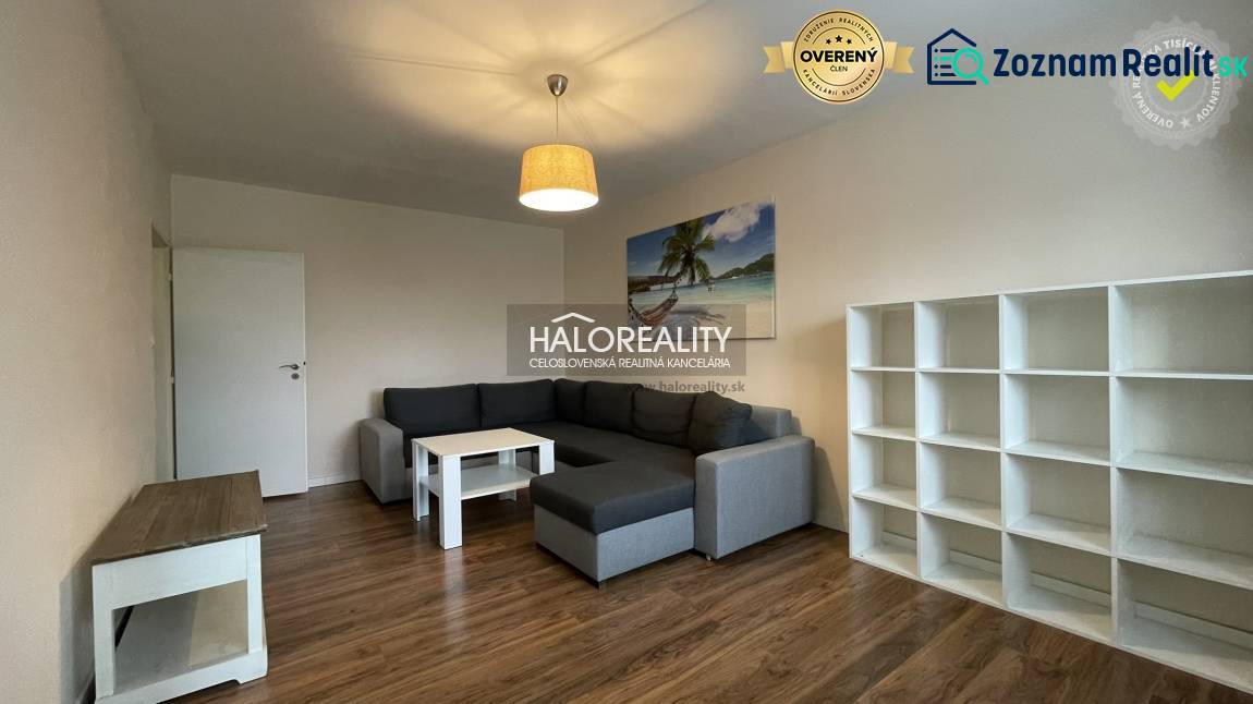 Living room with wood-patterned flooring in a three-room apartment, gray sofa, shelves.