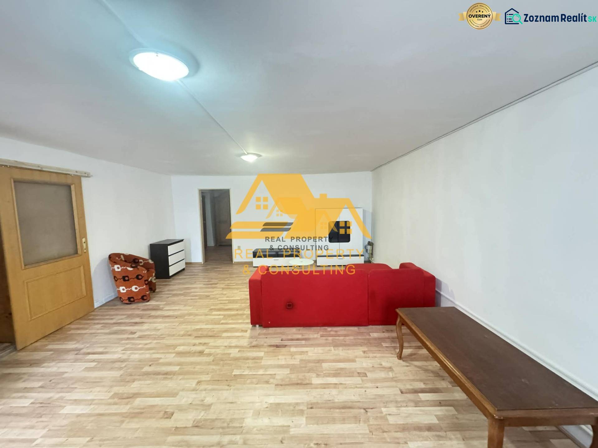 Living room in a two-room apartment with a wooden decor floor and a red sofa.