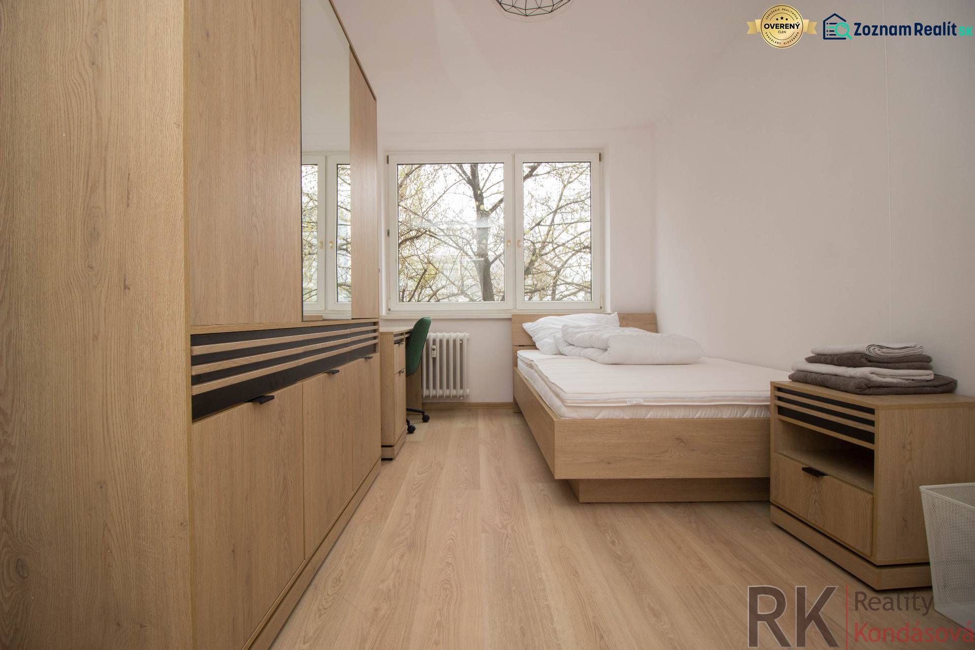 Bright bedroom in a three-room apartment with wood-patterned flooring and large windows.