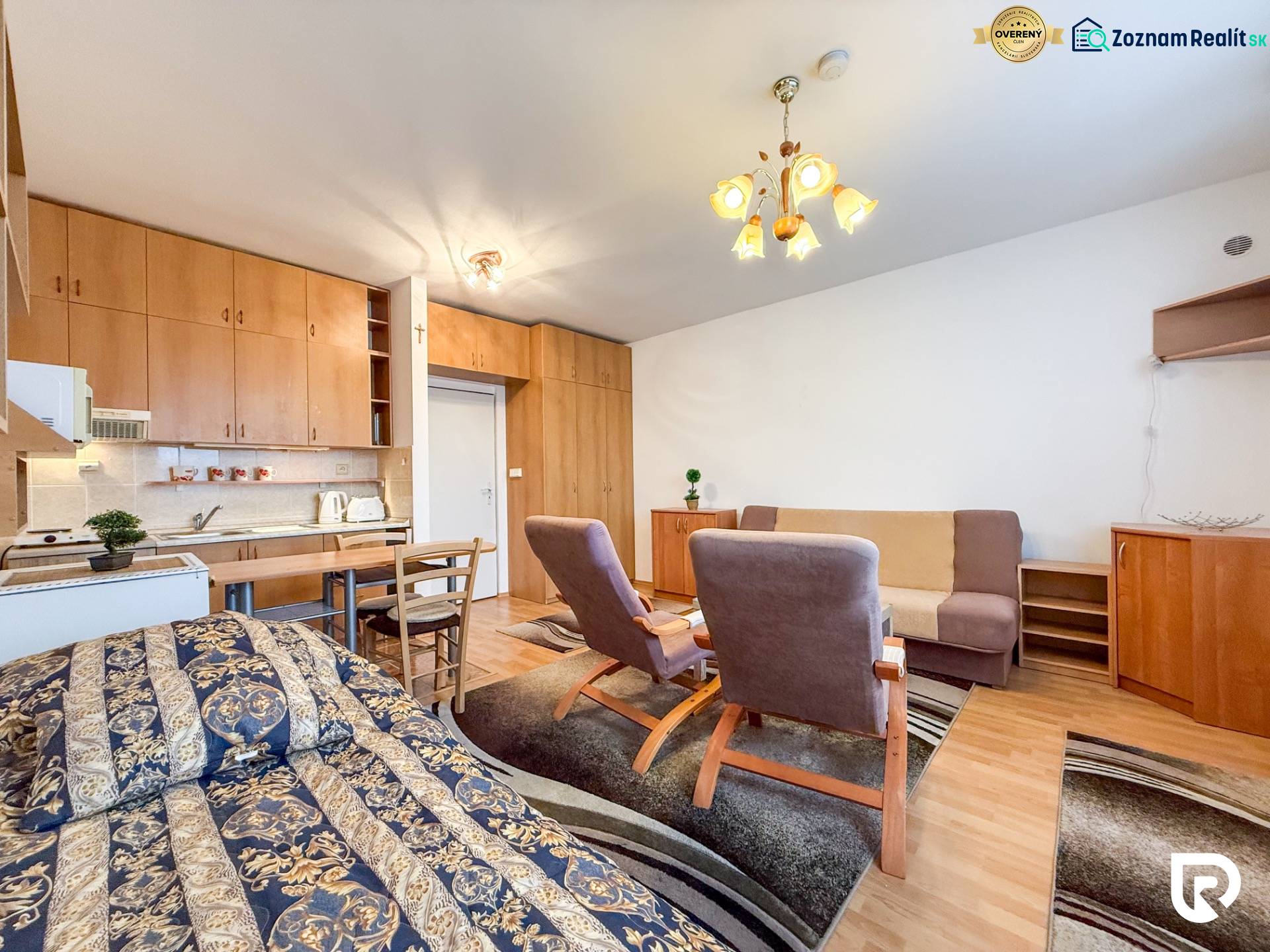 Studio apartment with a bed, kitchenette, and wood-patterned flooring.