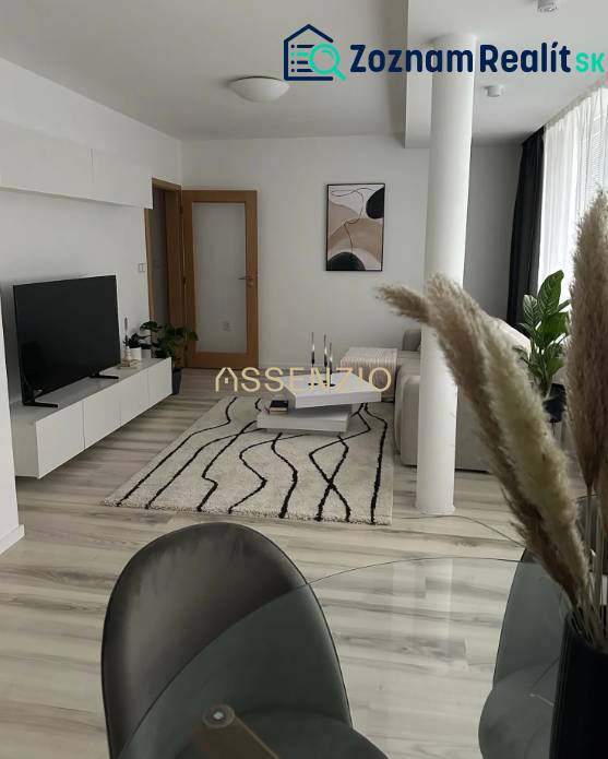 Living room of a two-room apartment with a wooden decor floor, white furniture, and a carpet.