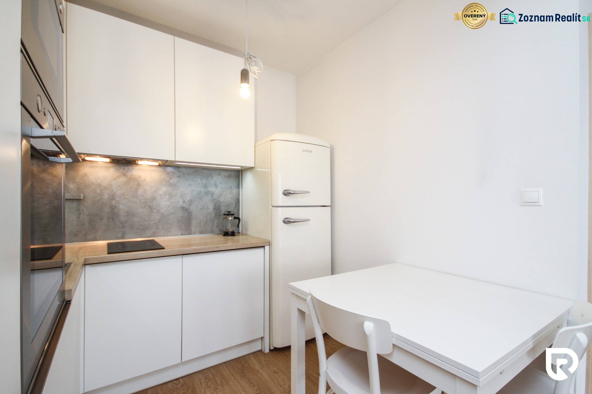 A kitchen in a 2-room apartment with white furnishings and a wood-patterned floor.