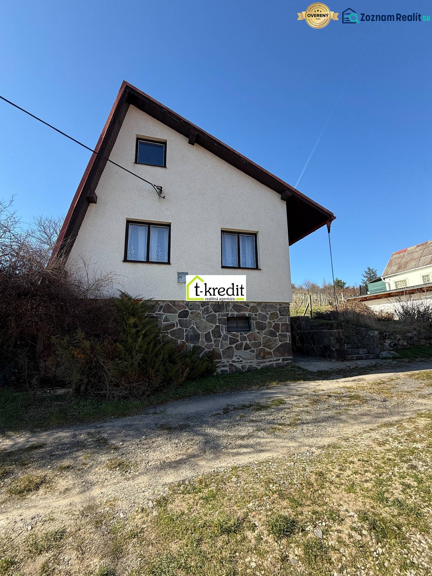 A cottage in Zlaté Moravce with a stone foundation and a sloped roof under a blue sky.
