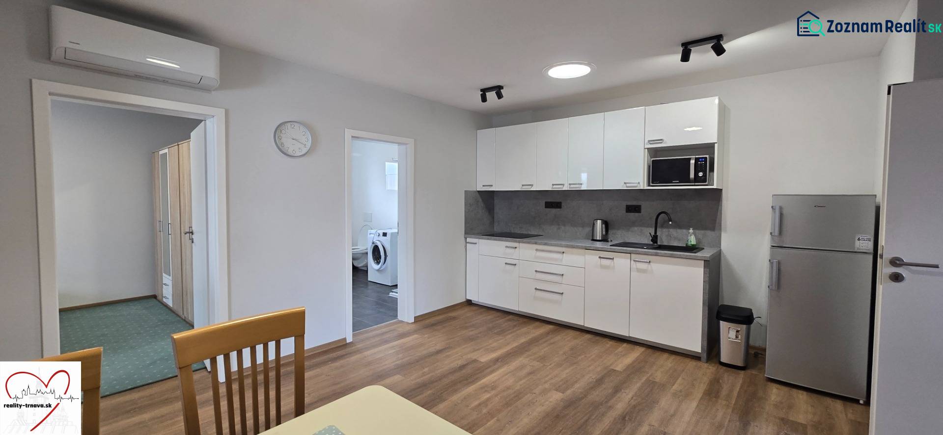 A kitchen with white cabinets and appliances in a 3-room apartment, with a wood-patterned floor.