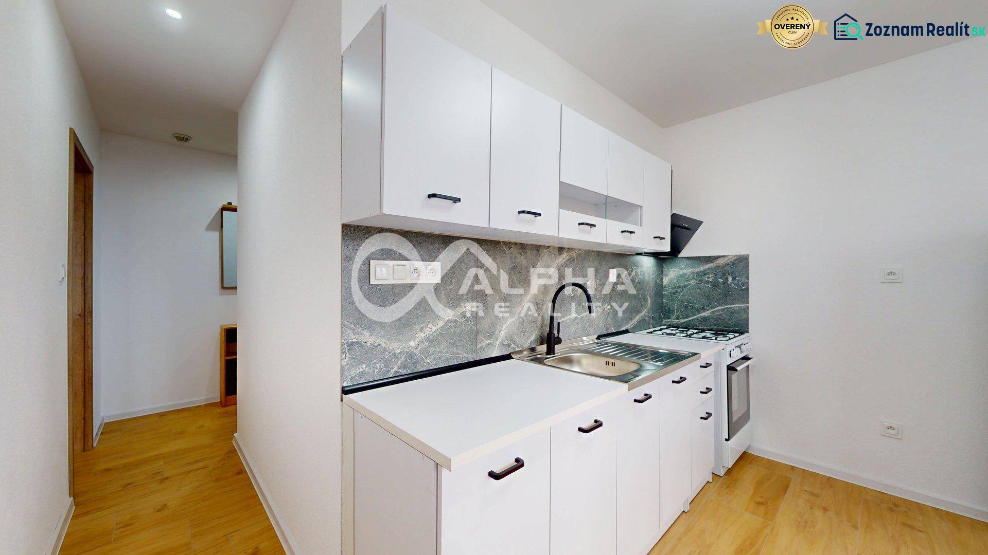 A kitchen in a studio apartment with white cabinets and wood-patterned flooring.