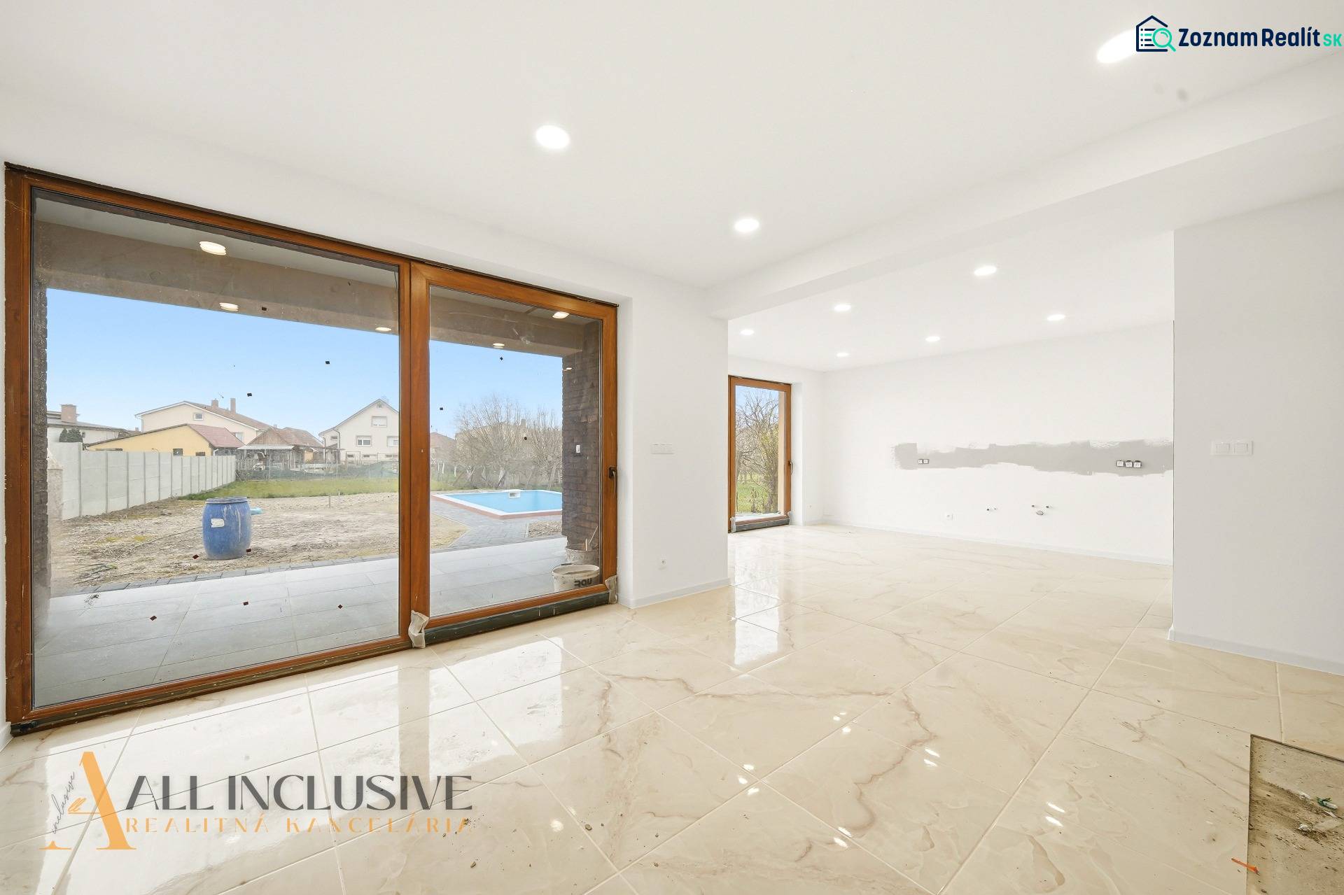 A spacious interior of a family house with large windows and a view of the garden with a swimming pool.