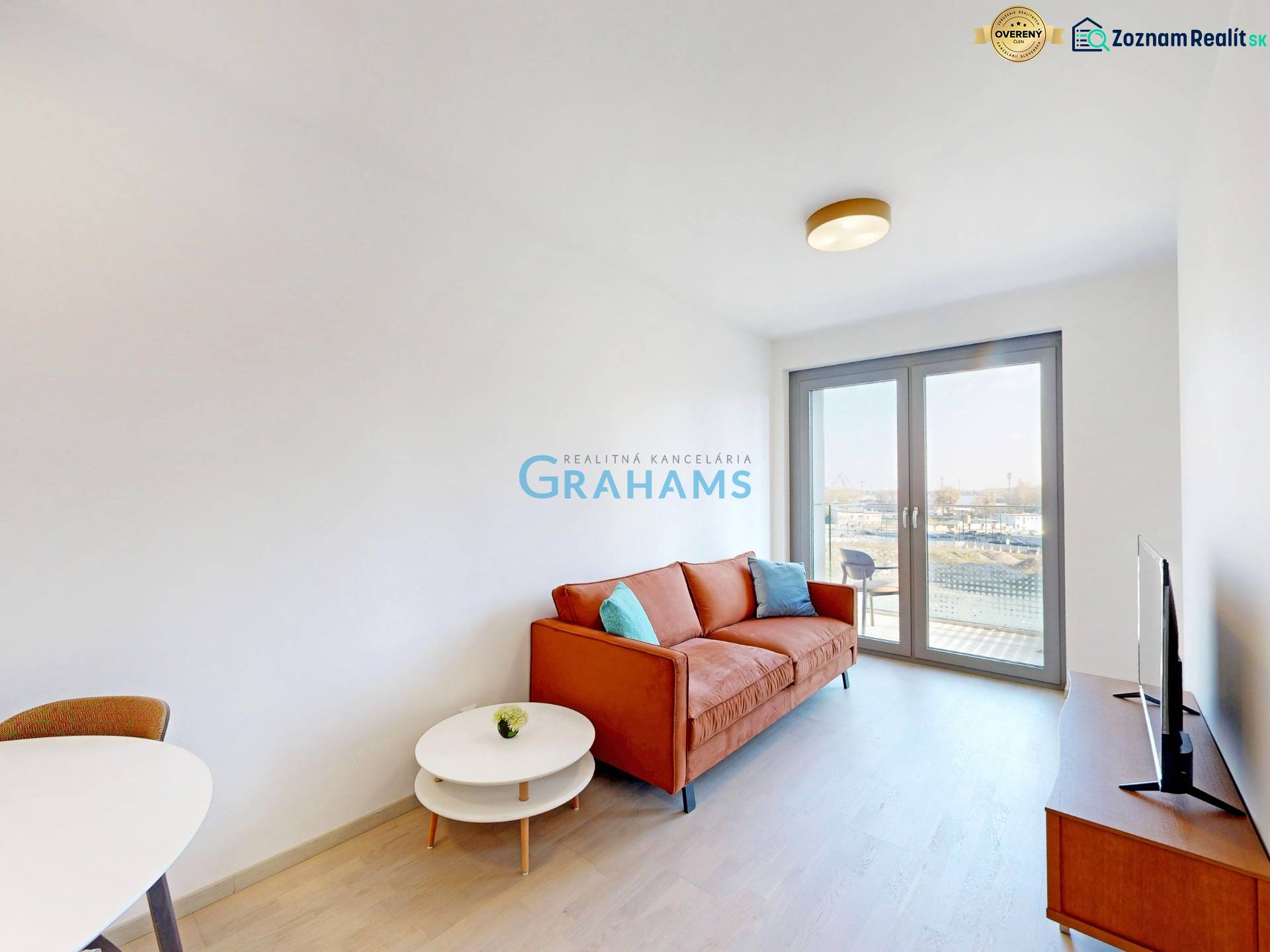 Living room in a two-room apartment with an orange sofa, TV, and balcony doors.