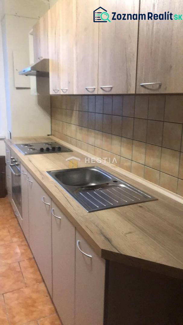 A kitchen in a 2-room apartment with a wooden decor floor and light furniture.