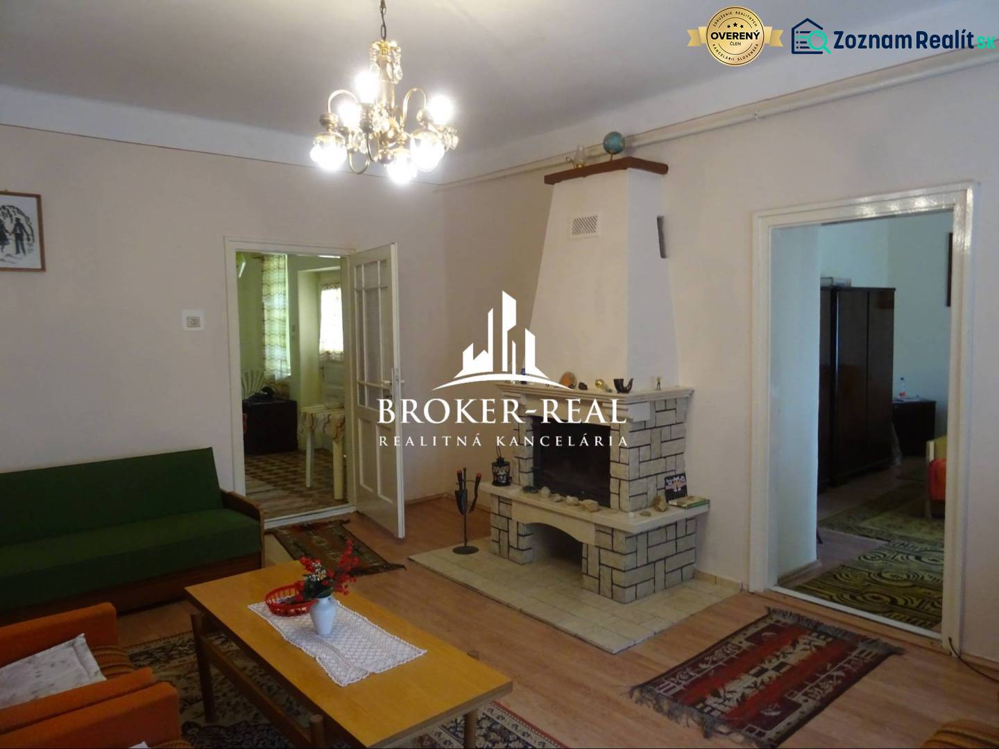 Living room in a family house with a fireplace, wood-patterned flooring, and a chandelier.