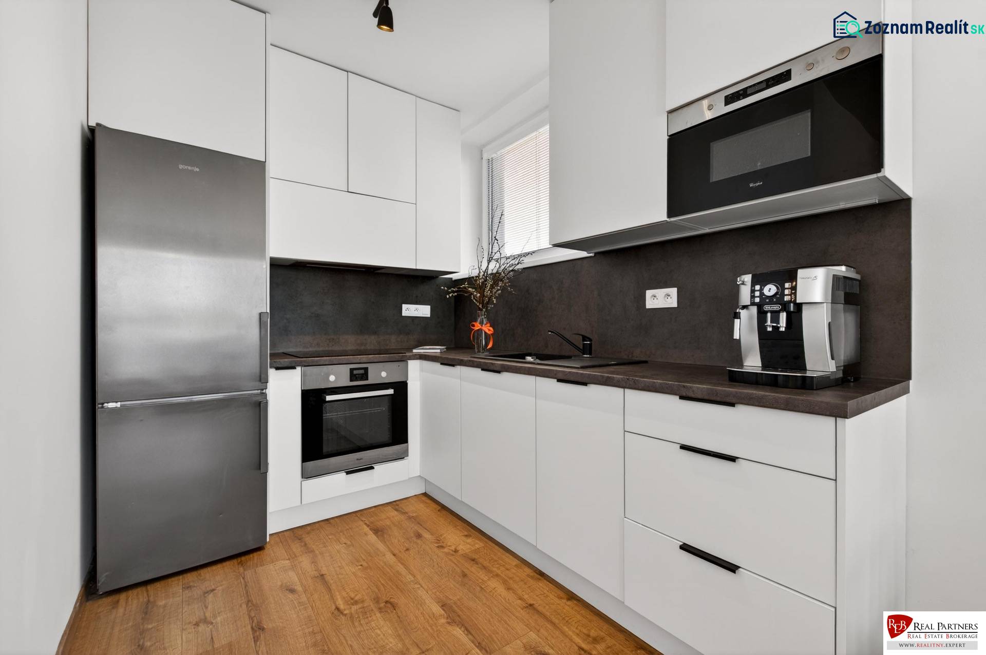 A kitchen in a 2-room apartment with a wood-patterned floor, white cabinets, appliances.