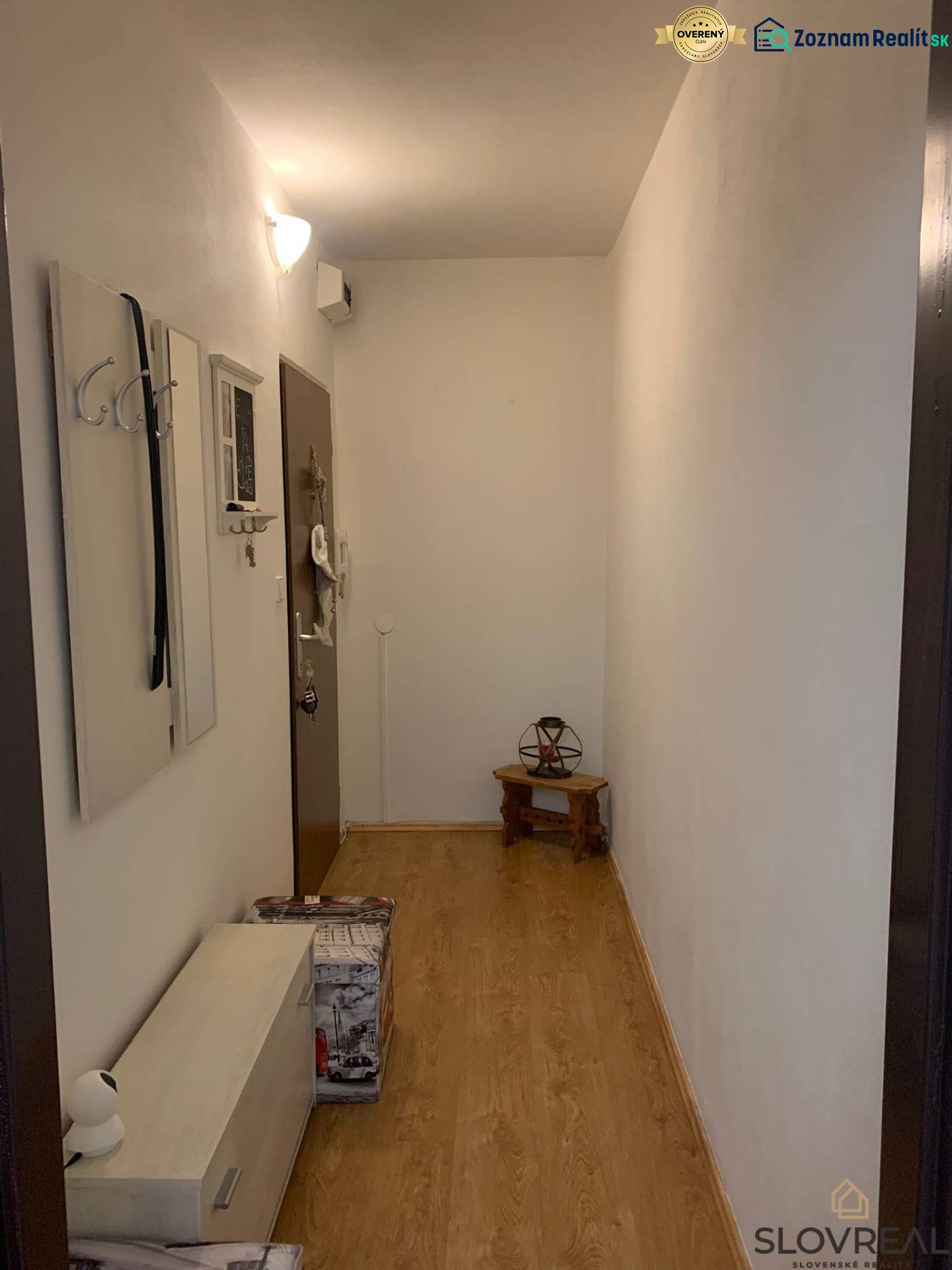 A narrow hallway with white walls, a wooden decor floor, and minimalist furniture.