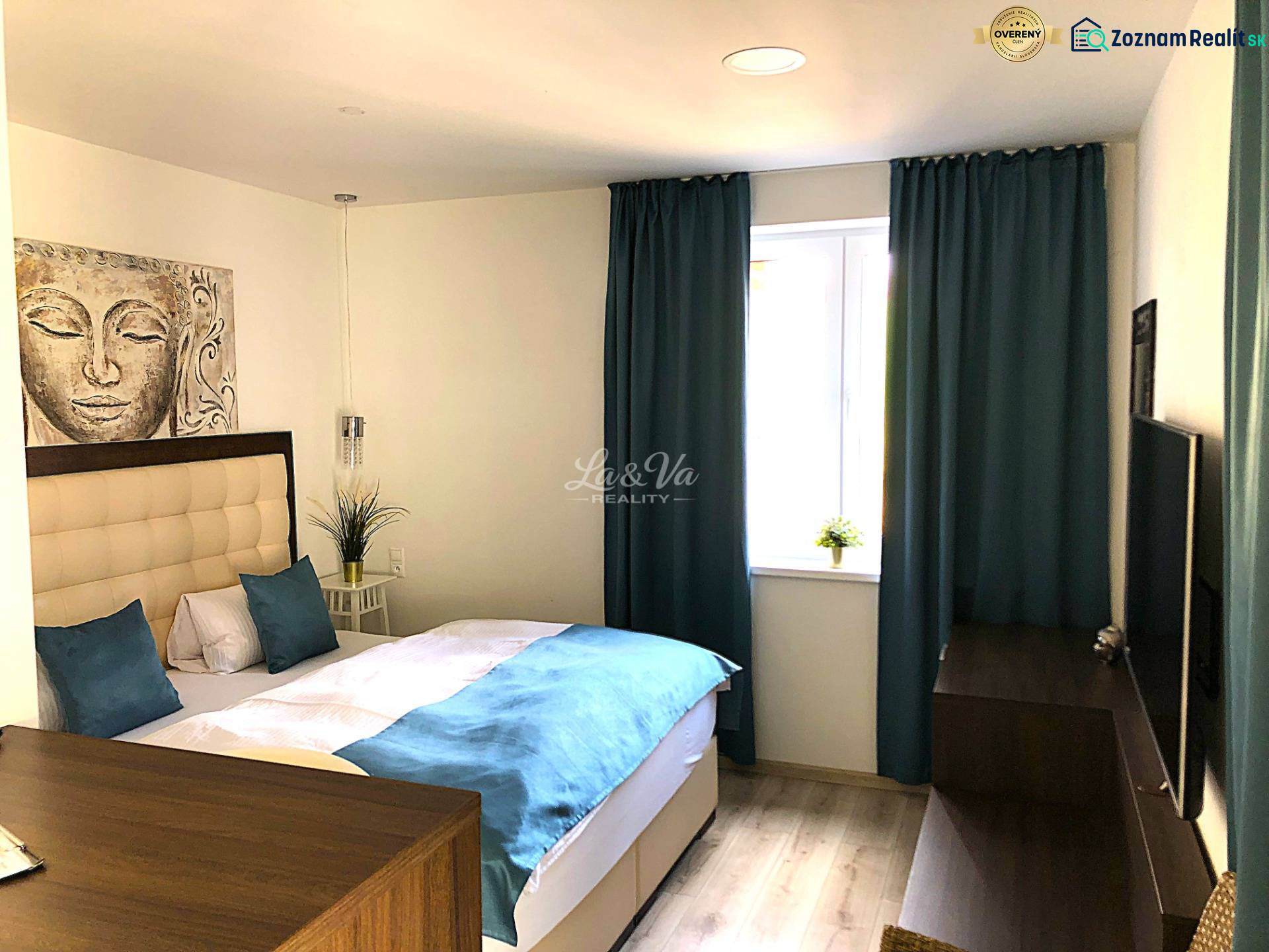 A studio apartment with light furniture, a bed, and blue curtains, with a wooden decor floor.