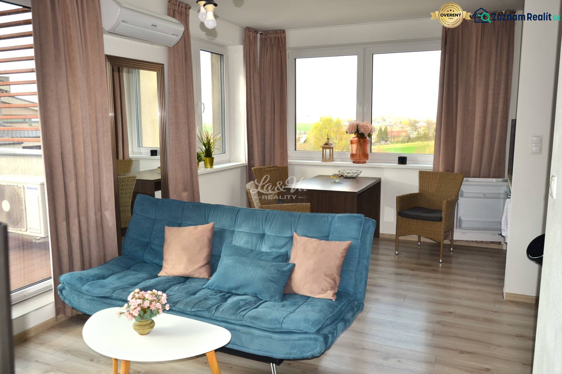 Living room with a sofa, table, plants, and a wooden-patterned floor in a two-room apartment.