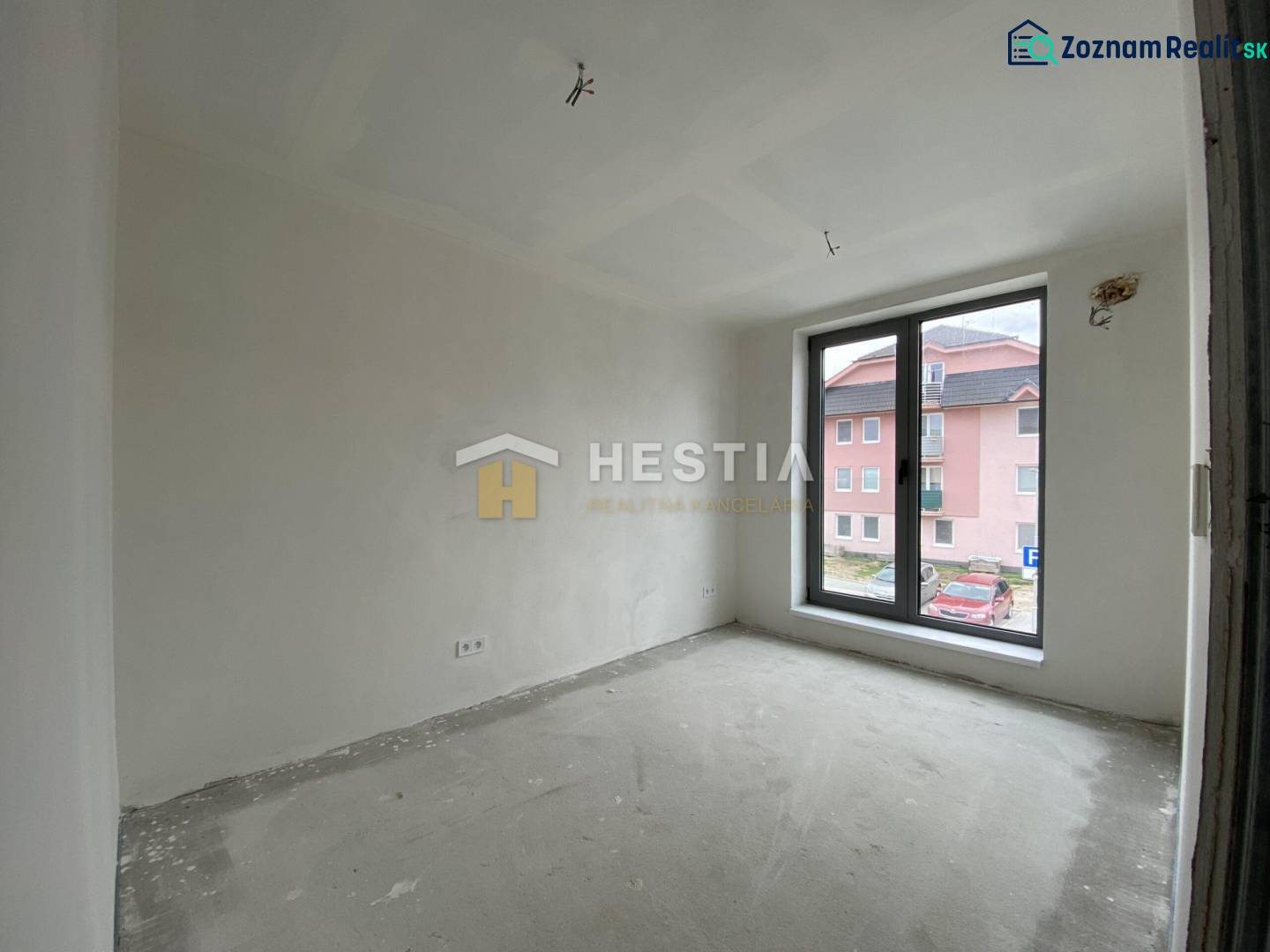 A room in a 2-room apartment with a raw floor and a large window overlooking the street.