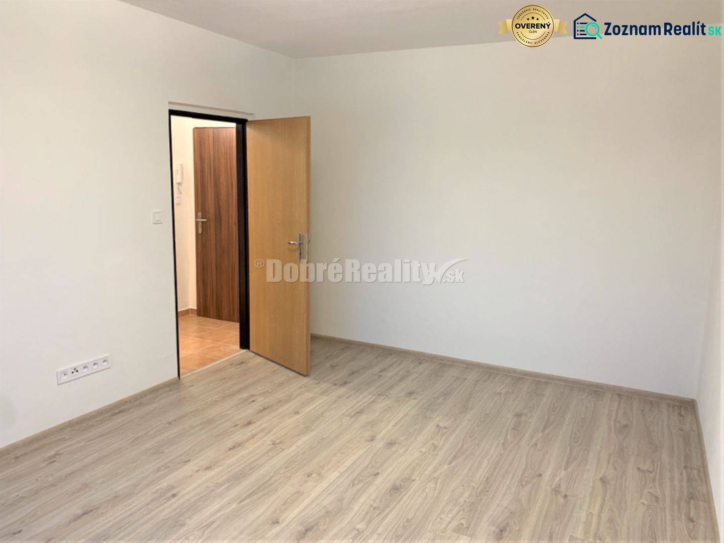 A room in a one-room apartment with white walls and a wooden decor floor.