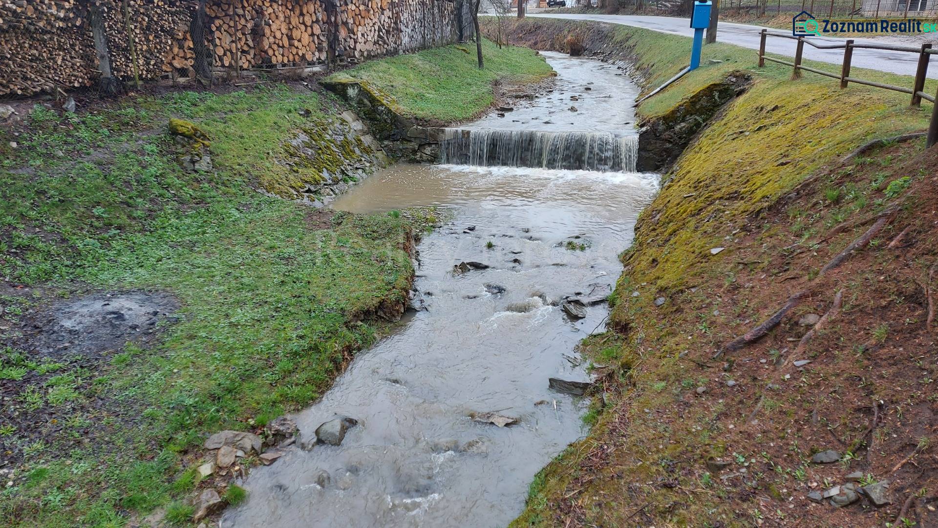 A stream flowing through recreational lands in Púchov with wood stored on the edge.