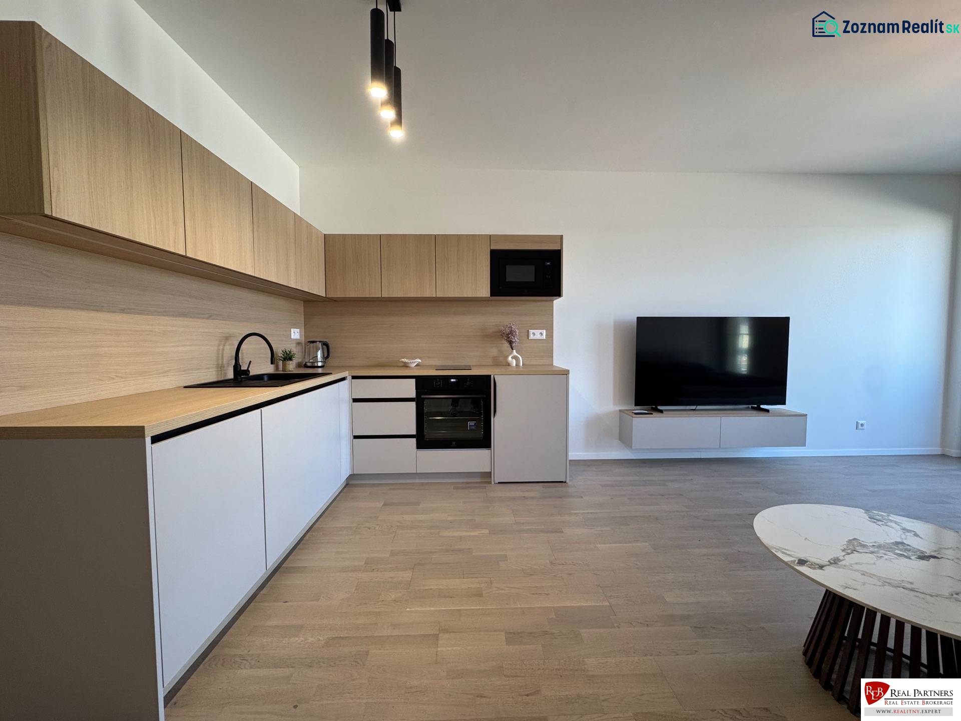 Kitchen in a studio apartment with wood-patterned flooring and a TV on the wall.