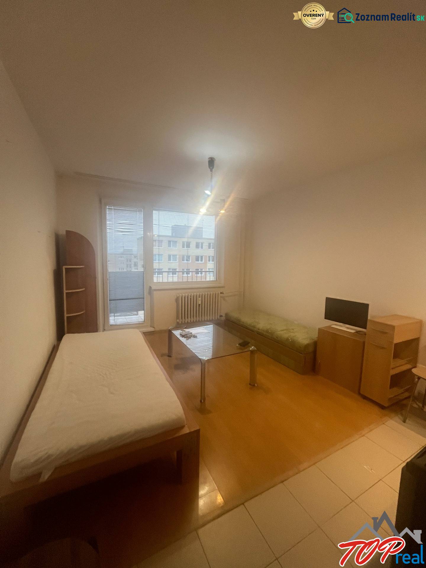 A studio apartment with a wooden floor, a bed, a sofa, and a table, simple interior.