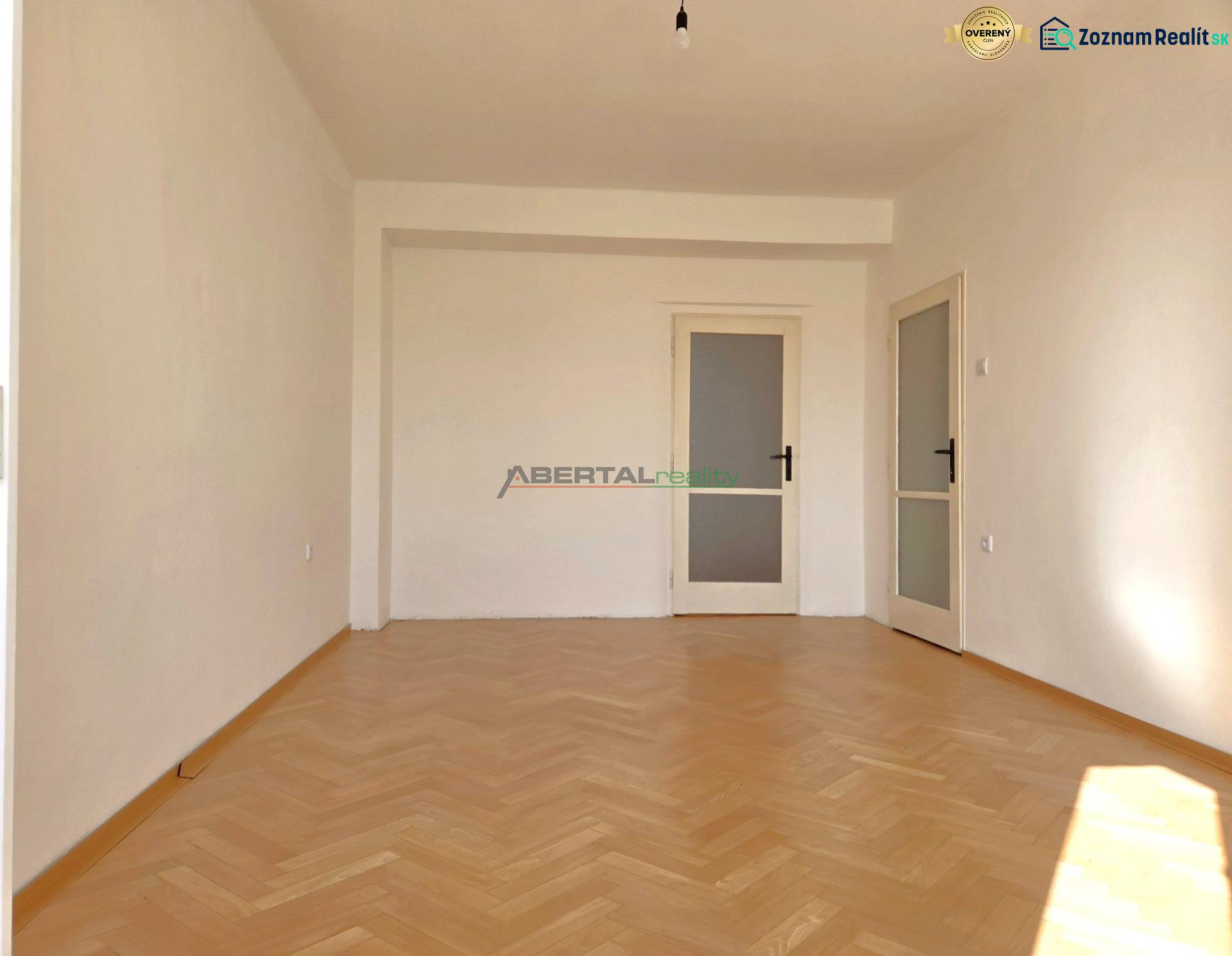 A room in a 3-room apartment has a wooden decor floor and white walls.