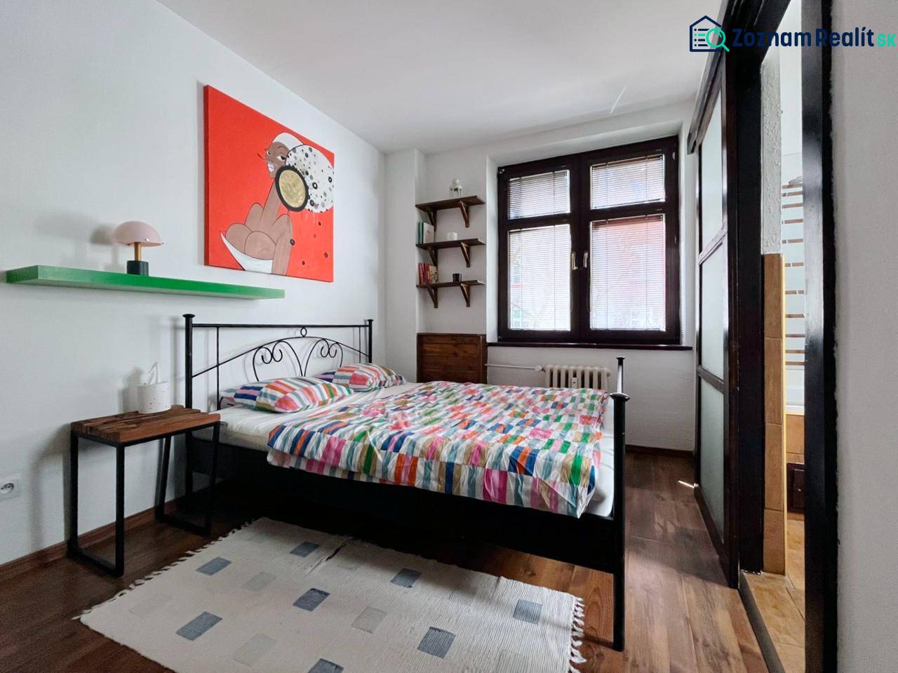 Bedroom in a 2-room apartment with a bed, painting, and floor with wood decor.