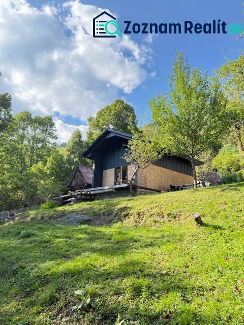 A cottage in Horná Mariková surrounded by green trees on a sunny slope under a blue sky.