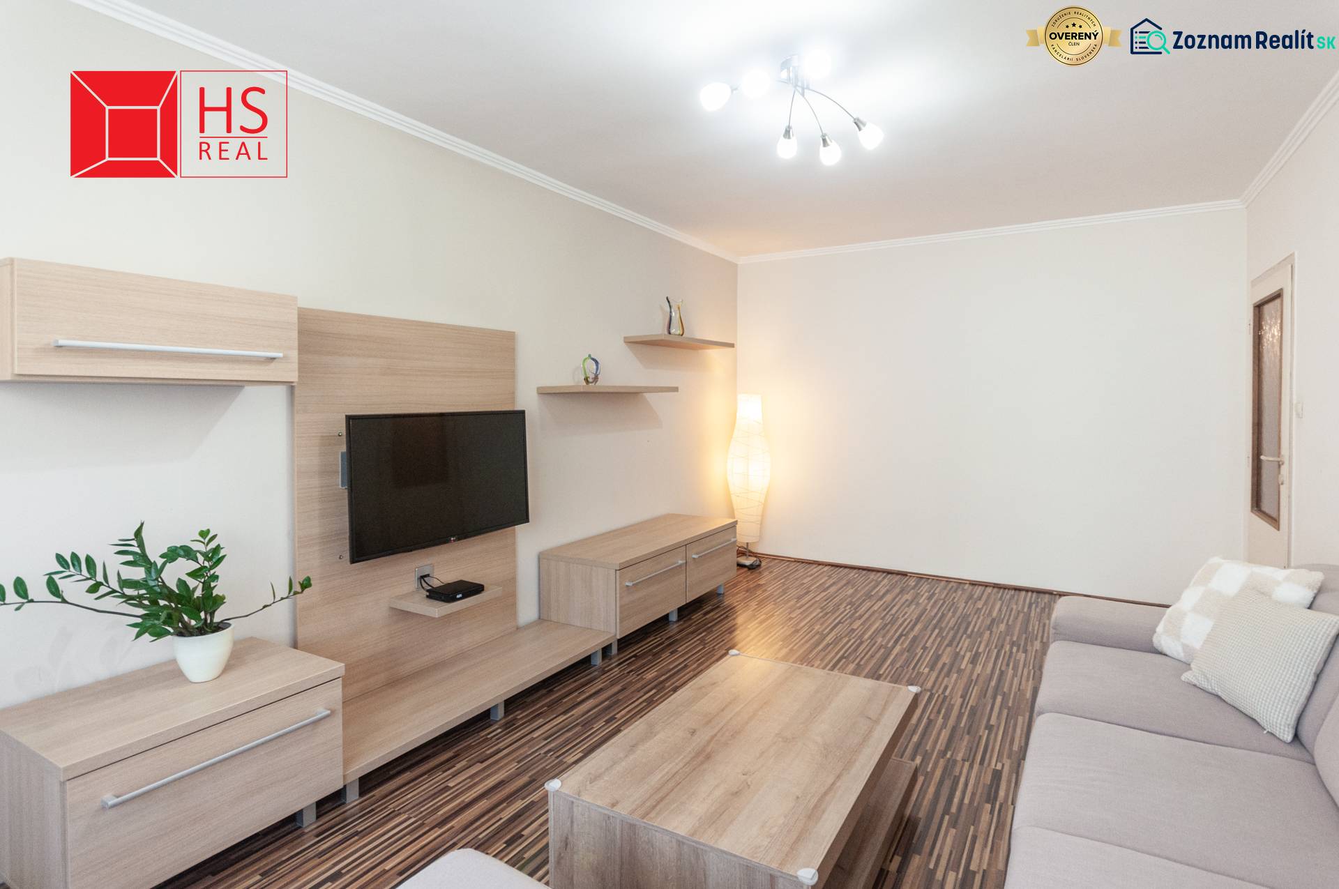 Living room of a three-room apartment with a wooden decor floor and a gray sofa.