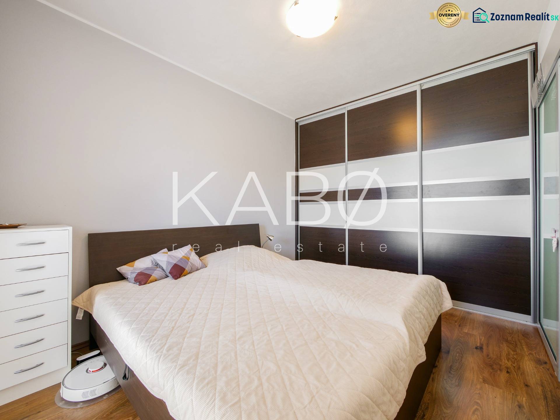 A bedroom in a three-room apartment with a wooden decor floor and a built-in wardrobe.