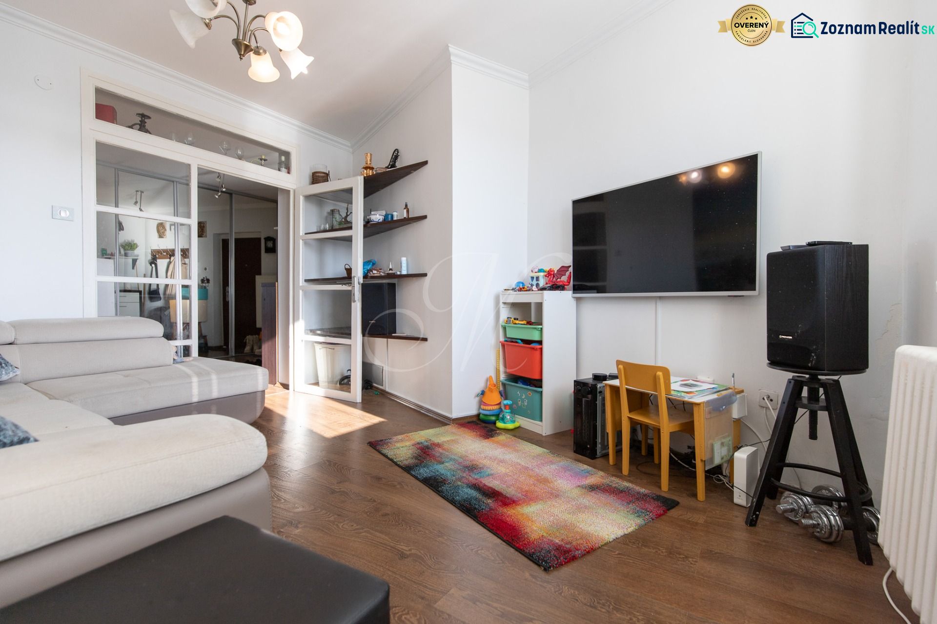 Living room in a two-room apartment with a sofa, TV, children's corner, and floor with wooden decor.