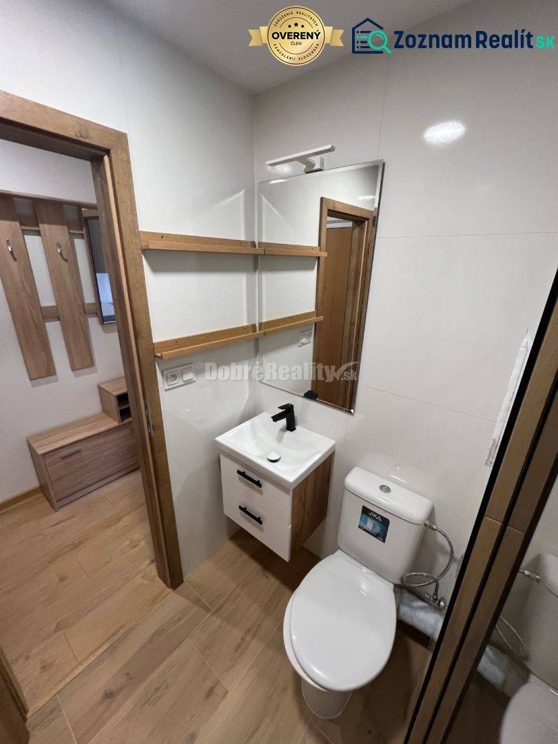 A studio apartment with a wooden floor, a small bathroom with a mirror and a sink.