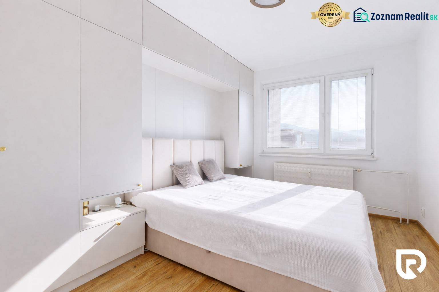 A bedroom in a 3-room apartment with a wood-patterned floor, white furniture, and a large window.