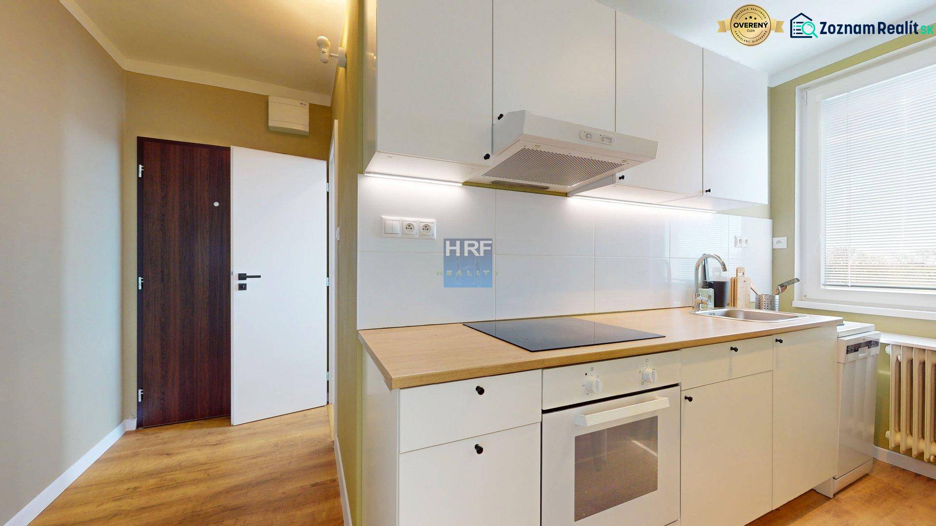Kitchen in a studio apartment with white cabinets, wood-patterned flooring, refrigerator, stovetop.
