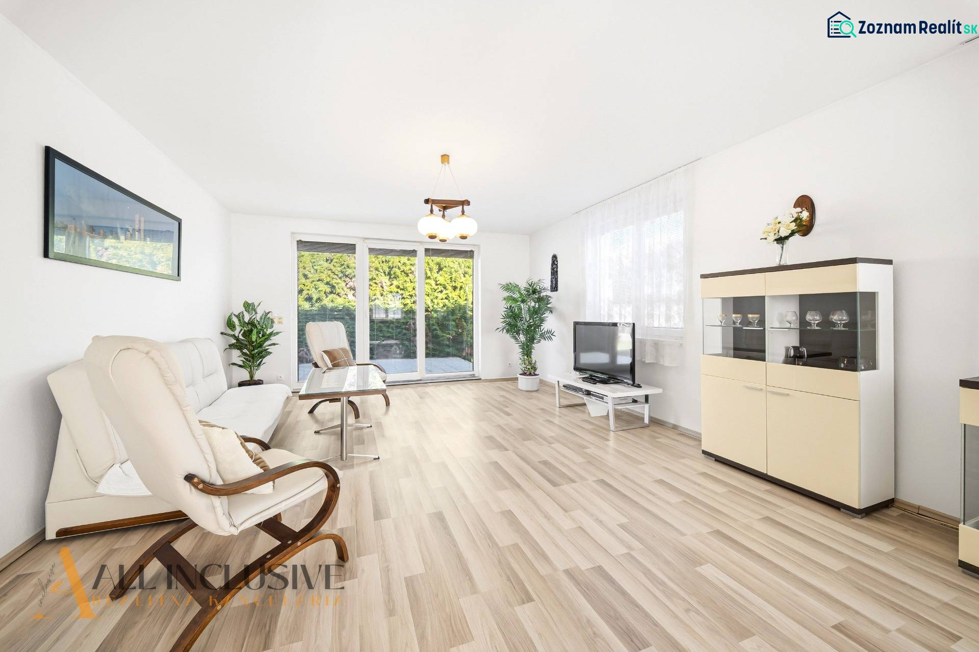 A bright living room with wood-patterned flooring, a sofa, an armchair, and a television.