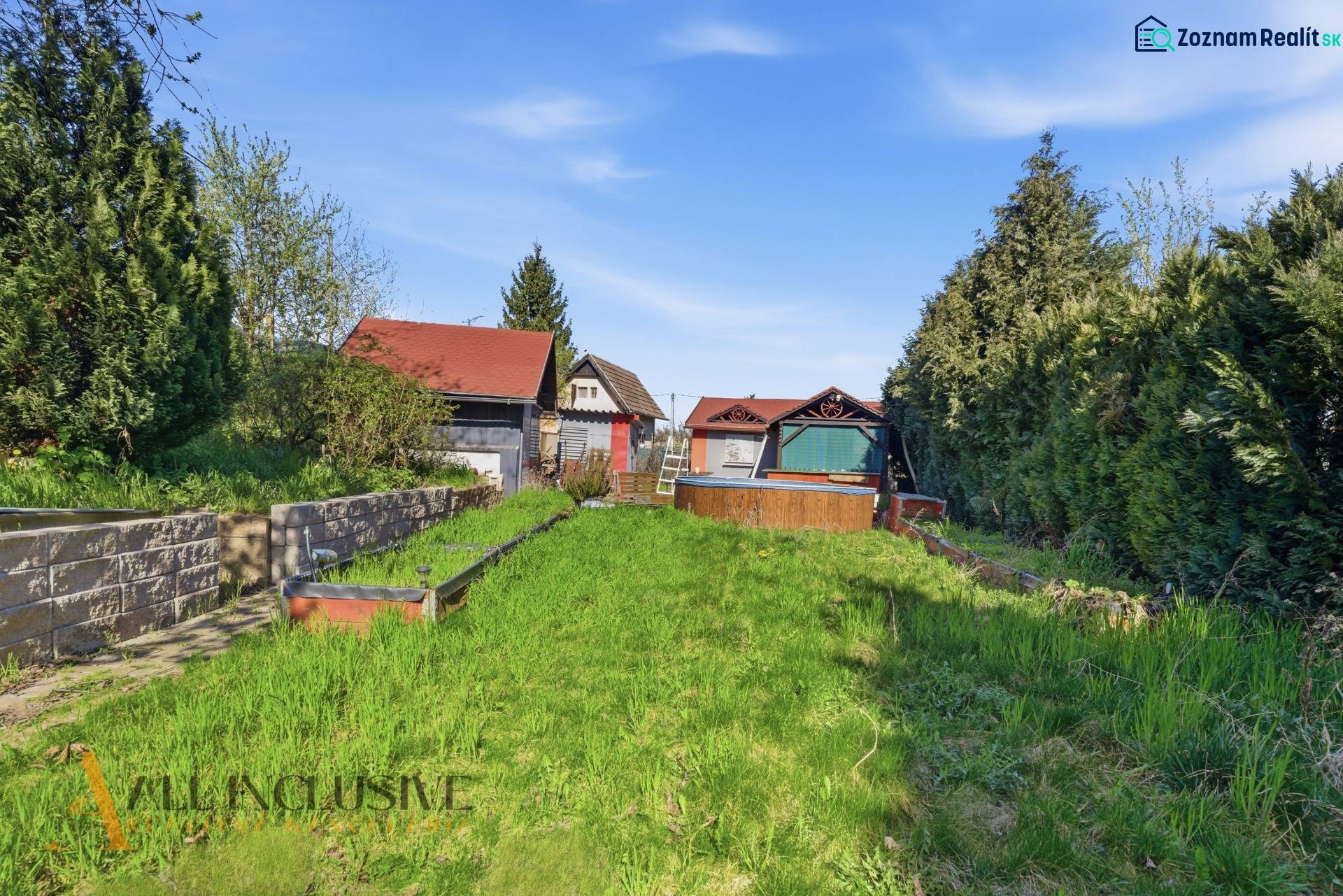 Gardens in Kráľová nad Váhom with a cottage, dense vegetation, and a lawn under the blue sky.